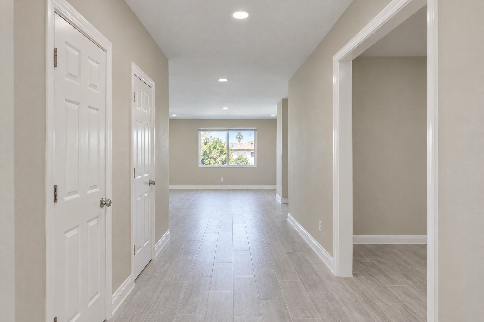Hallway after repainting: soft light greige walls, white ceiling, bright white doors, frames and baseboards
