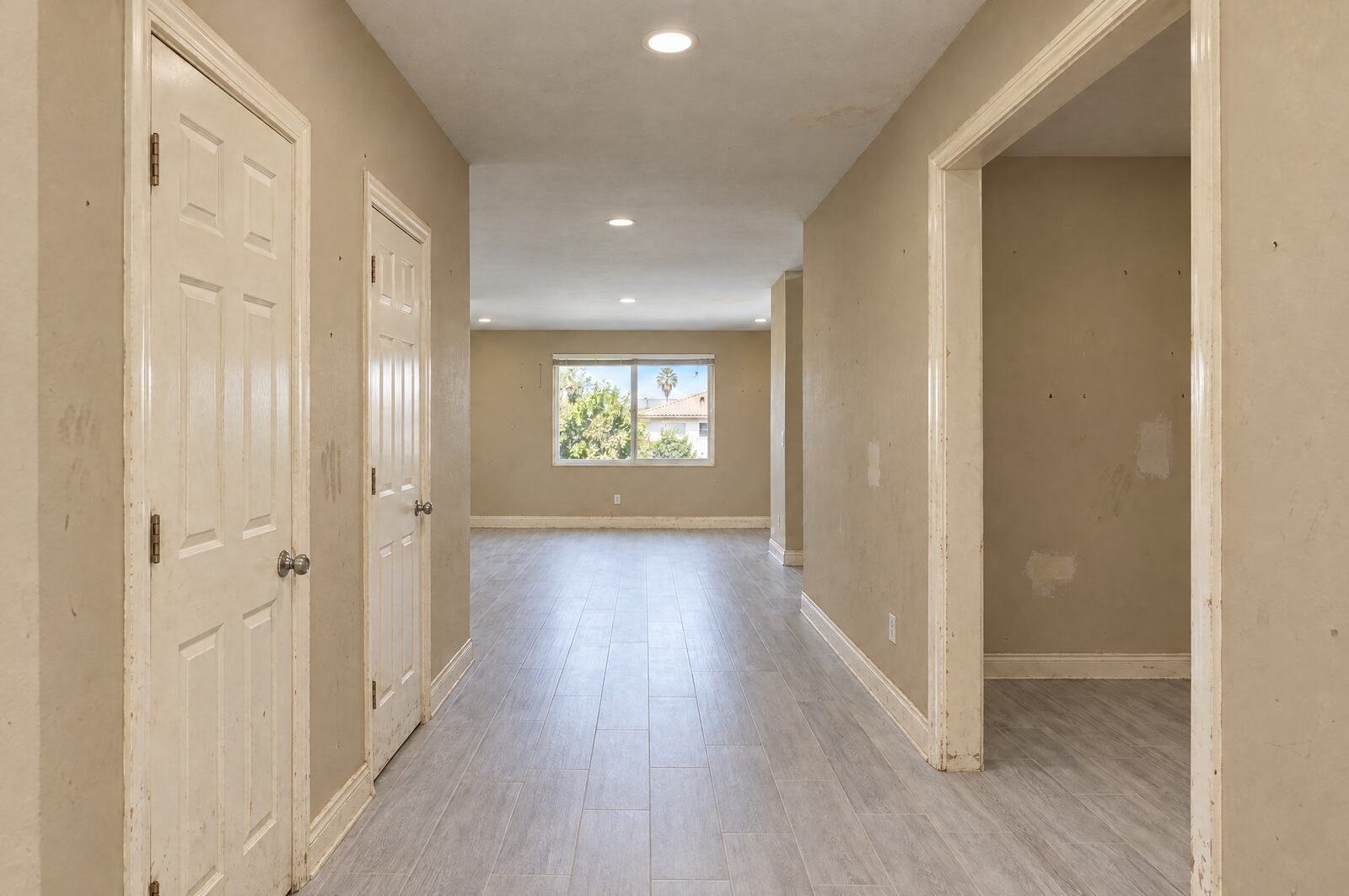 The same hallway before: dingy tan walls with scuffs and patch marks, yellowed and chipped doors and baseboards