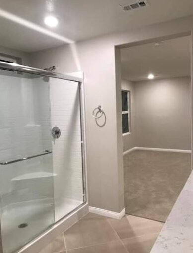 Bathroom with a glass shower opening into a bedroom, all walls freshly painted greige