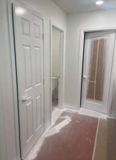 Hallway with freshly painted white doors, a glass door masked with paper, and the floor covered