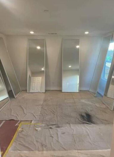 Bedroom with mirrored closet doors removed and leaned against the walls, floor covered with drop cloths